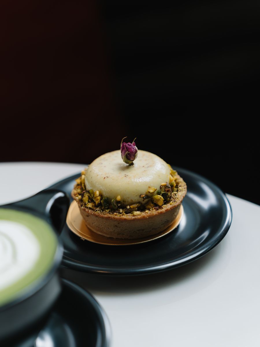 A pastry topped with a rosebud beside a matcha latte