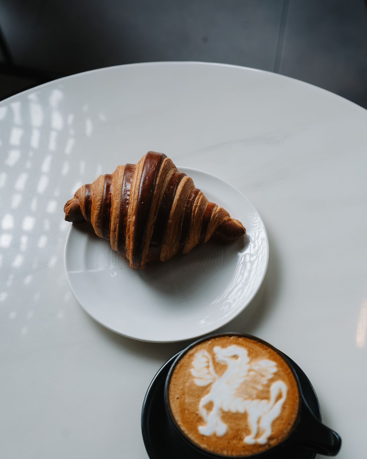 A croissant and a latte with latte art on a marble table at Momento Café